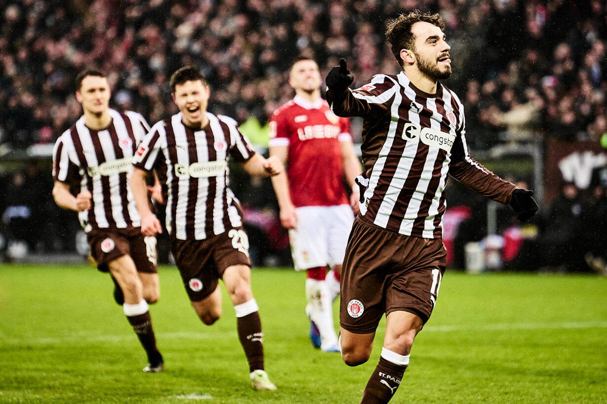 Danel Sinani vom FC St. Pauli jubelt über ein Tor, während seine Teamkollegen im Hintergrund begeistert mitlaufen.