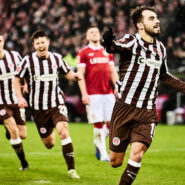 Danel Sinani vom FC St. Pauli jubelt über ein Tor, während seine Teamkollegen im Hintergrund begeistert mitlaufen.