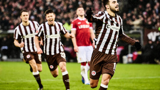 Danel Sinani vom FC St. Pauli jubelt über ein Tor, während seine Teamkollegen im Hintergrund begeistert mitlaufen.