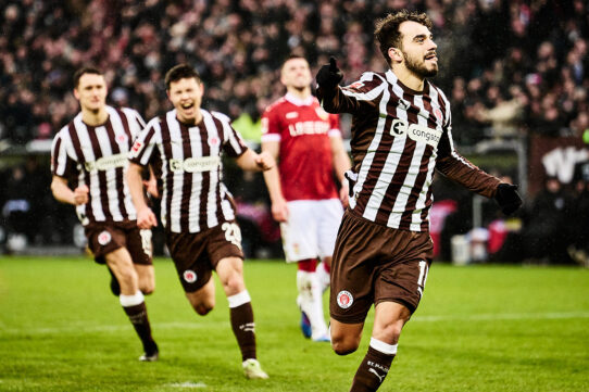 Danel Sinani vom FC St. Pauli jubelt über ein Tor, während seine Teamkollegen im Hintergrund begeistert mitlaufen.