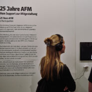 Zwei Besucher hören aufmerksam einer Präsentation über die 25-jährige Geschichte der AFM des FC St. Pauli zu.