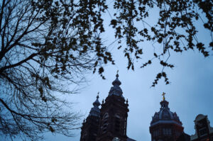 Die beeindruckenden Türme der Basilika St. Nikolaus in Amsterdam sind von zarten Blättern umrahmt, während der Himmel dunkel wird.