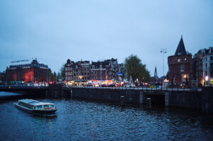 Eine beleuchtete Bootsfahrt gleitet durch die Grachten von Amsterdam, während die Stadt im Abendlicht erstrahlt.