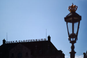 Ein eleganter Straßenlaterne im Vordergrund rahmt das markante Peek & Cloppenburg-Gebäude in Amsterdam ein. Schönes Beispiel der Schärfe einer Mandler Linse.