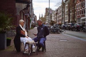 Zwei Personen sitzen entspannt an einem kleinen Tisch in Amsterdam, während sie Kaffee genießen und sich unterhalten. Schönes Beispiel der Zeichnung einer Mandler Linse.