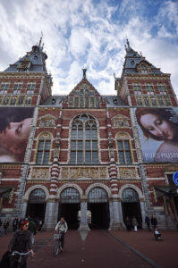 Die beeindruckende Fassade des Rijksmuseums in Amsterdam zieht Passanten an, während Radfahrende durch das Gebäude fahren können