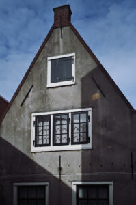 Ein graues Haus in Amsterdam mit einem charakteristischen Dach und einem Fenster, das von Schatten umgeben ist. Schönes Beispiel der Zeichnung einer Mandler Linse.