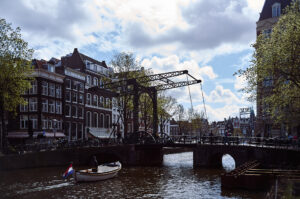 Ein Boot fährt unter einer historischen Brücke in Amsterdam, umgeben von charmanten Gebäuden und grünen Bäumen.